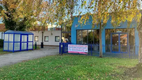 Images shows exterior of the one-story blue and white building, which also has some green grass in front.
