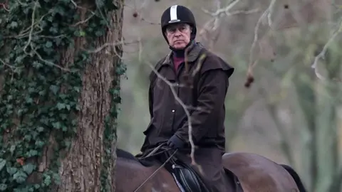 Reuters Close up of Andrew, wearing a riding helmet and a brown jacket, on horseback in a park.