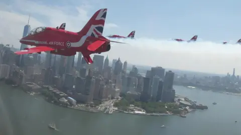 A red Royal Air Force plane flies over the New York City skyline.