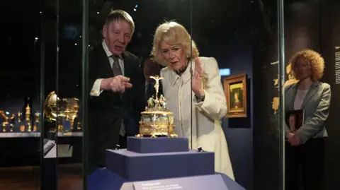 PA The queen is being shown an artefact by a man wearing a black suit. They are both looking at a gold artifact