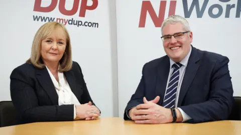 DUP Michelle McIlveen and Gavin Robinson sitting at a brown table. Both wear suits.