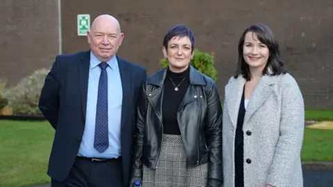 Michael Stoney - a bald headed man in a blue suit and tie,  justice secretary Angela Constance - short dark hair and black leather jacket and Rebecca Boundy of Kier Construction - shoulder length dark hair and a grey coat - smile directly into the camera