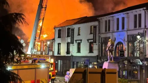 Joe Pugh A fire truck and firefighters in Abergavenny town centre with the orange flames and plumes of smoke in the background