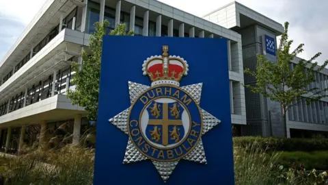 Outside Durham Police headquarters, with a close-up of blue sign which says Durham Constabulary and has a four lions symbol as well as the crown. 