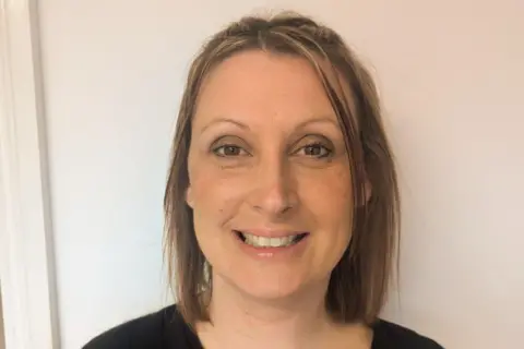 Lou Osborne Lou Osborne is shown in a head‑and‑shoulders portrait against a plain light-coloured background. She has straight, shoulder-length hair parted near the centre and is wearing a dark top. The person is facing the camera with a neutral expression.