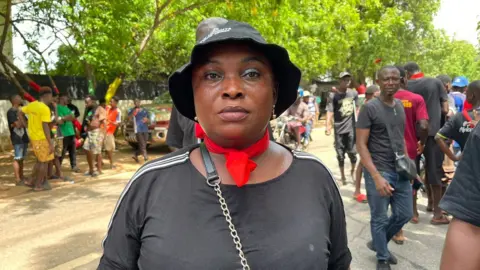 THOMAS NAADI / BBC Opposition protester Serwaa Akoto wears a black top, a black hat, and a red neckerchief.