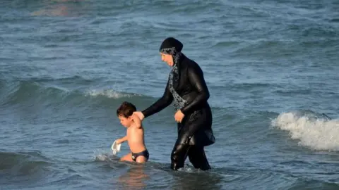 File photo of a woman wearing a burkini in the sea while holding the hand of a small child.