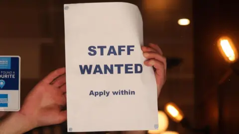 Sign being put up on a shop window that reads "STAFF WANTED Apply within"