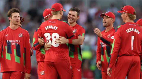 Jimmy Anderson (centre) is hugged by Mitch Stanley (STANLEY 38) with other Lancashire fielders around them after getting the wicket of Joe Root