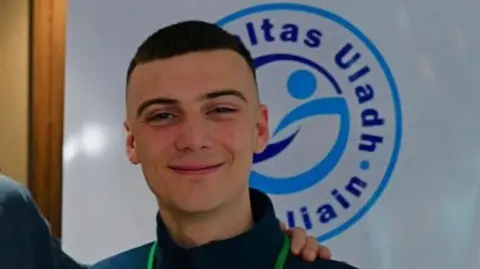 Eoghan Ó Conghaile Eoghan Ó Conghaile has short brown hair and is smiling at the camera. He is wearing a dark blue fleece top and a green lanyard can be seen around his neck.