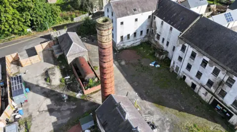 An aerial view of an old mill site in the Borders with an industrial chimney and dilapidated properties