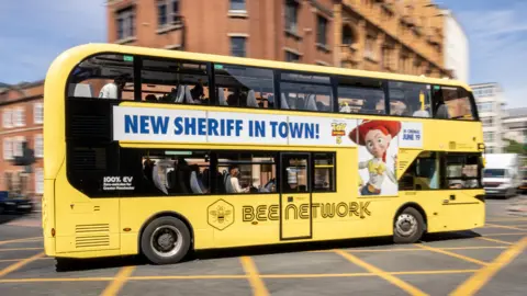 PA Media Yellow Bee Network bus in central Manchester sports an advert on the side for Toy Story 5. It contains the slogan "NEW SHERIFF IN TOWN!" as a pun for the Greater Manchester mayoral election.