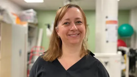 A woman with ginger hair and wearing surgical scrubs smiling at the camera.