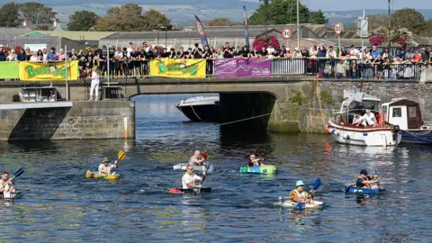 MANX SCENES Competitors setting off in Castletown Harbour. There are sponsorship banners on the harbour wall behind.