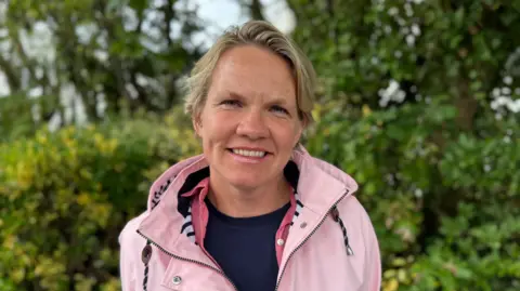 BBC A picture of Deputy Sasha Kazantseva-Miller. She is wearing a pink jacket and has blonde hair.