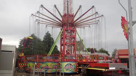 Red funfair ride with swings attached, trees visible in background