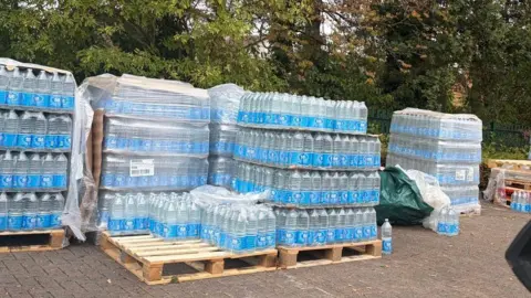 BBC News Stacks of bottled water on pallets are laid out in a school yard