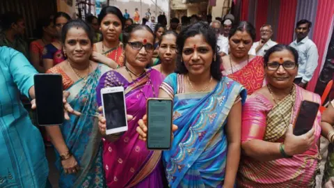 Hindustan Times via Getty Images : Women who were beneficiaries of mukhyamantri ladaki bahin yojana showing thier bank passbooks and the message of the scheme money received in thier mobile phones at Kisan Nagar on September 10, 2024 in Thane, India. The beneficiaries have recieved Rs three thousand in 2 months. (Photo by Praful Gangurde/Hindustan Times via Getty Images)