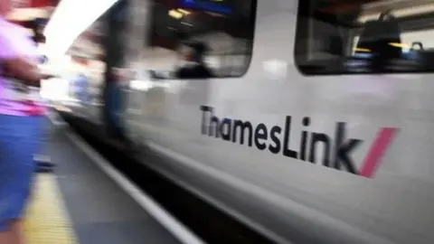 A Thameslink train blurred as it passes a station platform, 