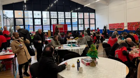 BBC Dozens of people are pictured, with many of them sitting at round tables. A number of people are wearing red tops.
