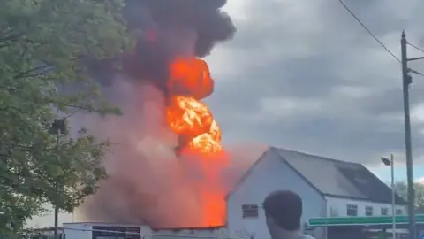A large fire impacting a building with billowing grey clouds