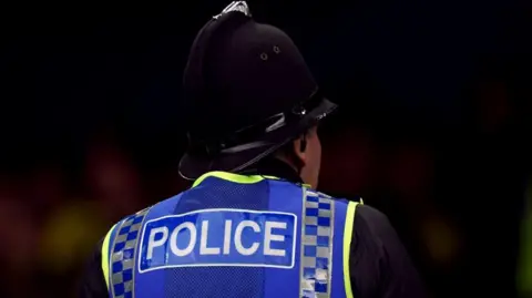 PA Media The back of a police officer, who is wearing a helmet and a high-vis jacket that says POLICE.
