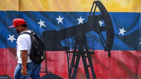 A man walks past a mural depicting an oil pumpjack, or 'nodding donkey' on a Venezuelan flag in the country's capital Caracas