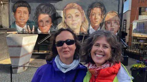 Turistas Pam Koekbakker e Tobi Wittonfotos em frente ao mural Derry Girls. 