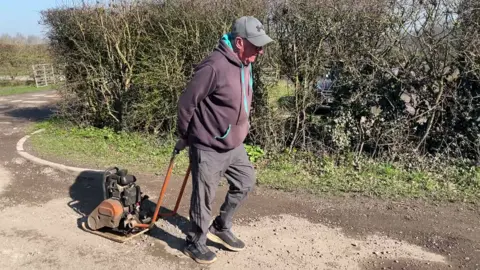 An older man pulling a wacker plate along a road.