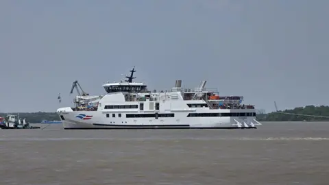 Isles of Scilly Steamship Group A general view of a large, white, passenger ferry. It is floating on still waters. 