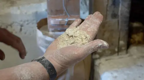 BBC/Oli Constable A miller at Worsbrough Mill in Barnsley puts grain into a hopper for it to be turned into flour.