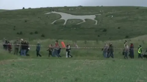 People walking down a path in front of a white horse on a hillside
