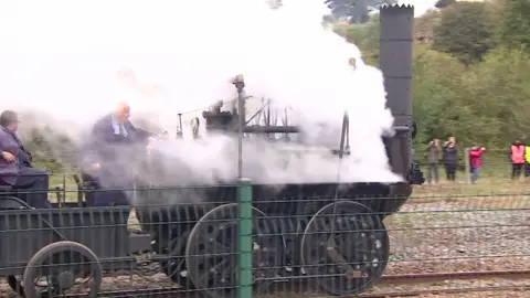 A replica of Locomotion 1 during the Stockton & Darlington Railway 200 Festival in 2025. The front of the engine is pouring out white steam while people look on taking photographs.