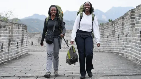 Two young women with large rucksacks and in hiking boots walk down the Great Wall of China