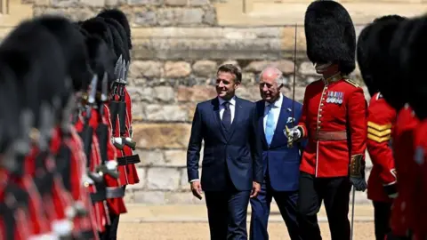 Getty Images Emmanuel Macron smiles as he inspects a guard of honour alongside King Charles. 