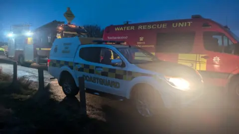 Berwick Coastguard Rescue Team Coastguard and fire service vehicles parked on a narrow road in the dim light. 