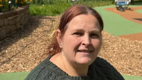 Samantha Goguelin is wearing a green jumper and a red hair, she is pictured in the playground in Parade Gardens 
