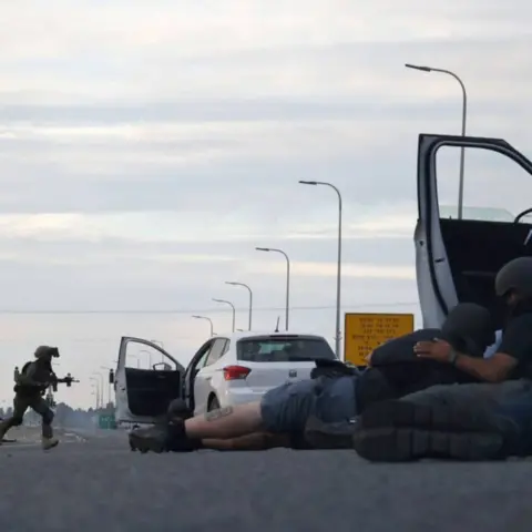 Getty Images Journalists take cover behind cars as Israeli soldiers take position during clashes with Palestinian fighters near the Gevim Kibbutz, close to the border with Gaza on 7 October, 2023