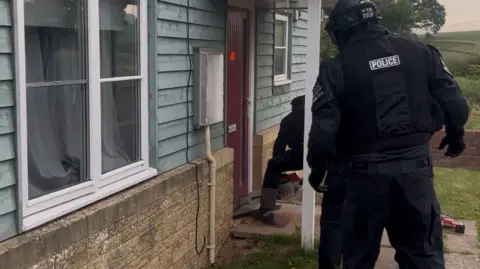 Police picture of a raid on a house. Two officers are visible in protective uniform gaining entry via the front door
