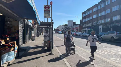 So-called floating bus stop shows the shelter, a cycle lane and the bus stop itself. A woman with a pushchair is awaiting a bus