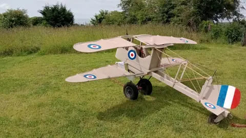 Margaret Snell A replica of a Vickers Gunbus bi-plane on a lawn. It is painted in a beige colour with a blue, red and white tail fin, in the same design as the French flag, and the circular RAF logo on each wing, the tail and the cockpit.