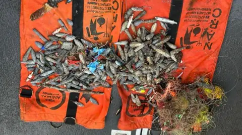 David Kennard/NARC A pile of angling materials, mostly fishing lines and baits, are presented on top of bright orange diving bags. 