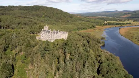 Strutt & Parker Aerial image of Carbisdale Castle on a tree-covered cliff overlooking a loch