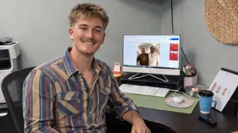 Cayden McBride poses for a photo as he sits in front of a computer