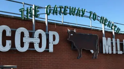 An image of "Co-op cow" sign placed on a brick wall on the side of Derby Central Hall