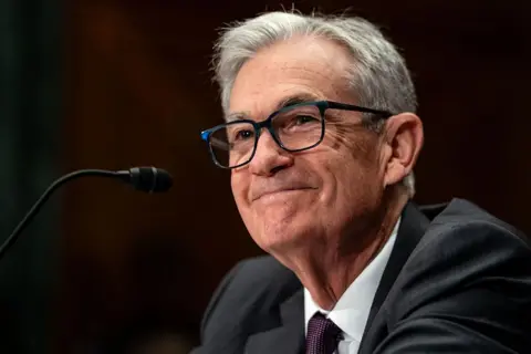 Getty Images Uśmiechnięty Jerome Powell, ubrany w ciemnoszary garnitur, siedzi przed mikrofonem