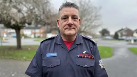 A man with grey hair in a navy fire and rescue shirt