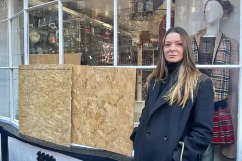 Maria standing outside a boarded up shop.