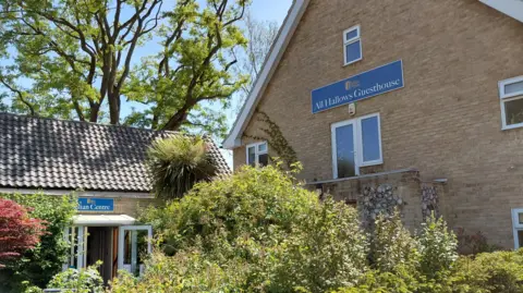Jamie Mann Pictured are the All Hallows Guesthouse and Julian Centre. There are two buildings with lush green foliage and bushes in front of them. A blue sign with white writing on one of the buildings says "All Hallows Guesthouse".