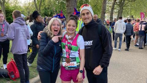 Ashley Delgado celebrates with her family after finishing the London Marathon as her mum points at her with her mouth open in excitement while her brother smiles at the camera